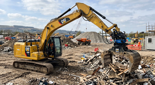 A yellow CAT excavator with a hydraulic rotator on its grapple on a construction site.