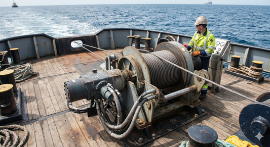 A detailed view of a large, industrial-grade hydraulic towing winch mounted on the weathered wooden deck of an offshore workboat.